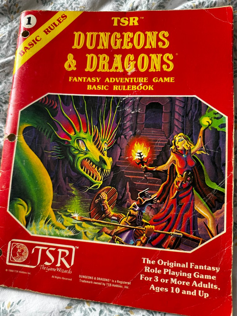 The cover of the Basic D&D set rule book. It has a red cover in some disrepair and has the same illustration as the cover of the box, A green serpent attacks a sorceress in red in dungeon surroundings.