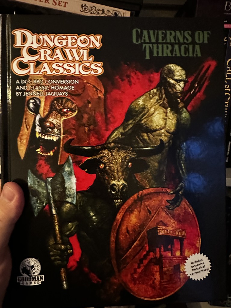 The cover of Dungeon Crawl Classics Caverns of Thracia. :arge face of a savage fighter in a bronze helm, lizard man in the background, Minotaur with axe and shield in the foreground.