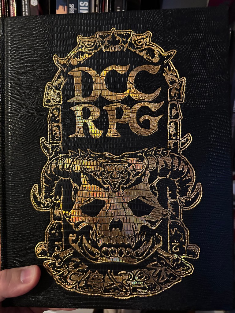 The Cover of the Special Edition of DCC RPG. it has a gold embossed demon skull complete with horns on the faux-leather black cover.