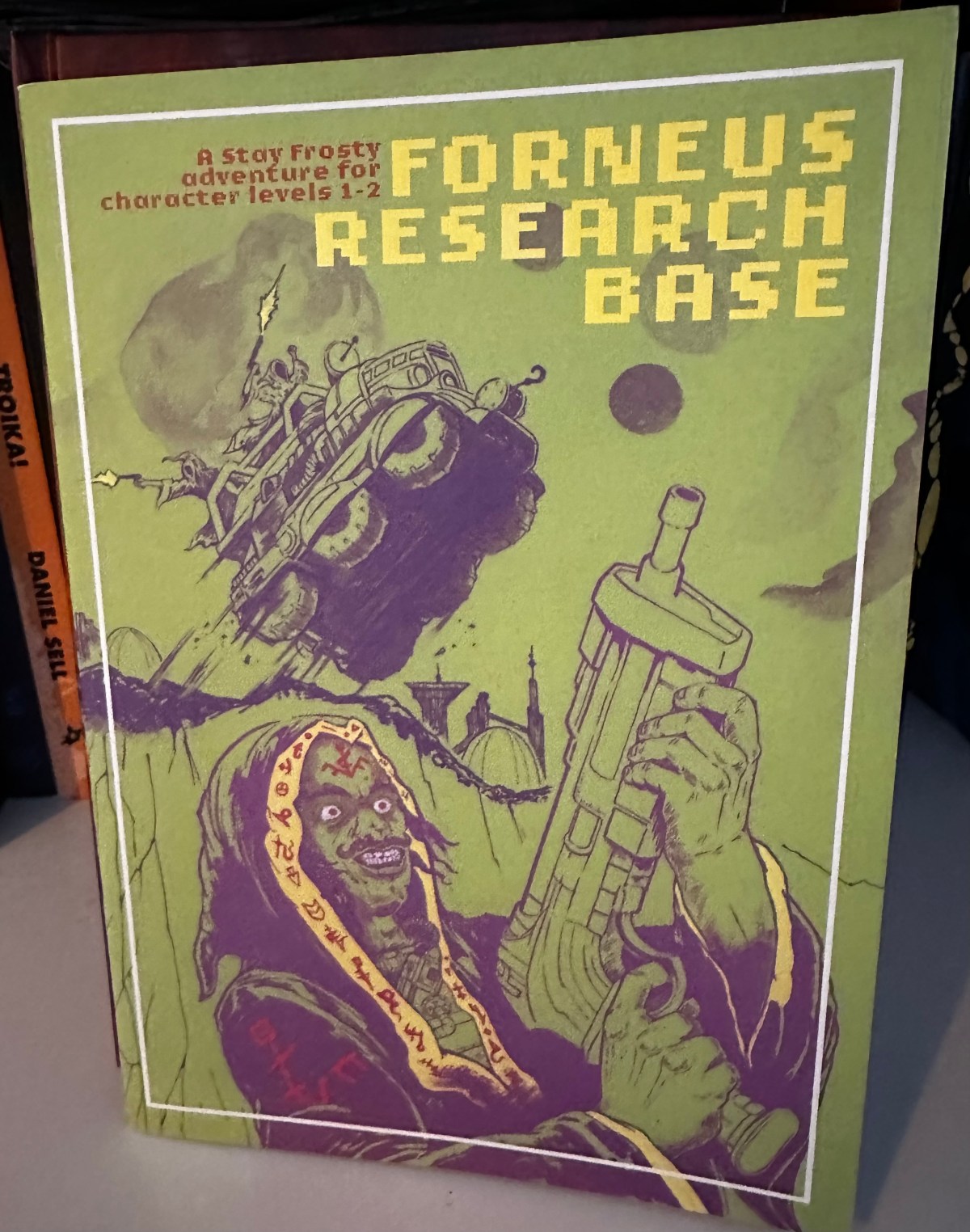 The cover of Forneus Research Base. Its very green and has a cultists with a gun and an ATV jumping from a hill on it.