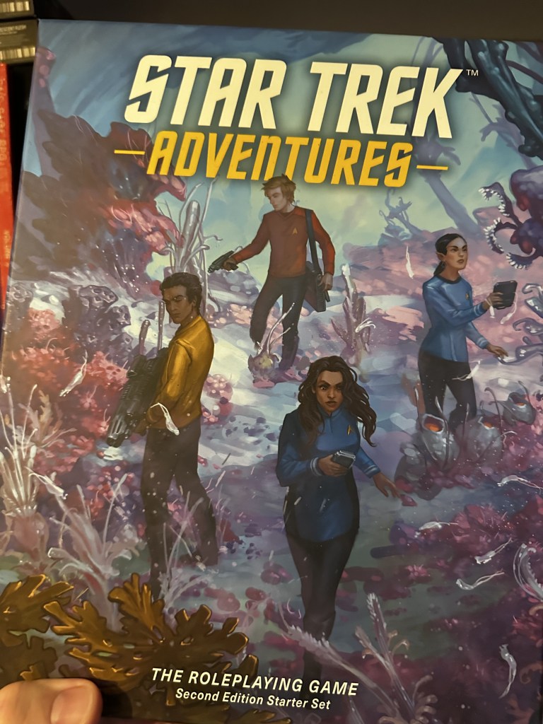 The cover of the Star Trek Adventures 2E Start Set Campaign Book. A variety of TOS era characters are gathered performing investigative tasks on a planet's surface.