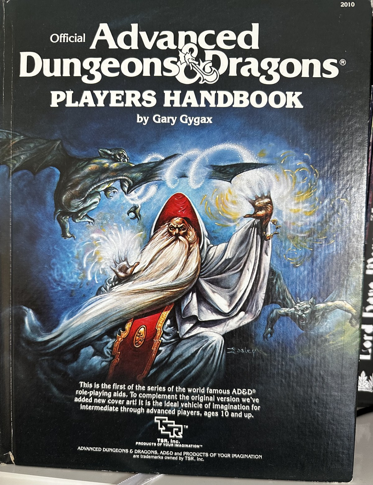AD&D 1st Edition Player's Handbook cover. Art by Jeff Easley. A wizard with a long, white beard and robes of white and red defends himself against some small, flying gargoyles.